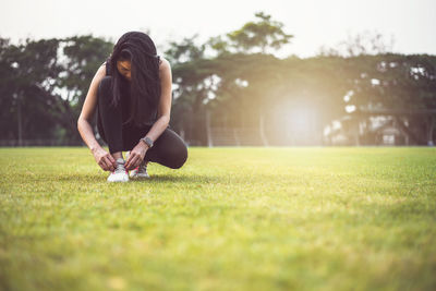 Full length of woman tying shoelace while crouching on land