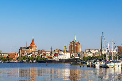 Buildings by river against clear blue sky