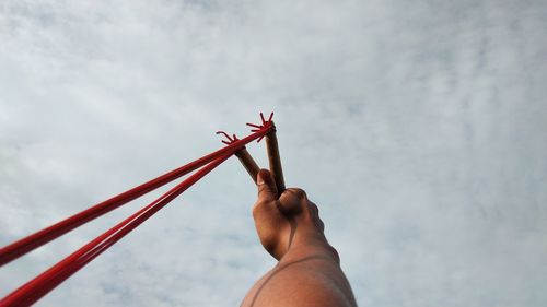 Close-up of hand holding red against sky