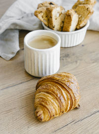 Freshly baked classic croissants and almond biscottis with cup of cappuccino on linen  background. 