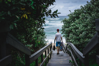 Rear view of man walking on footbridge at beach