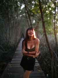 Sensuous young woman standing amidst trees on boardwalk at forest