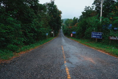 Empty road amidst trees in city against sky