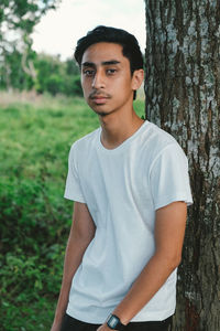 Portrait of young man standing against tree