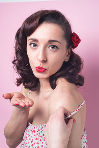 Portrait of sensual woman blowing kiss against pink background