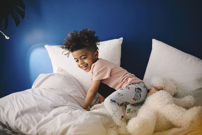 Happy boy playing with teddy bear on bed at home