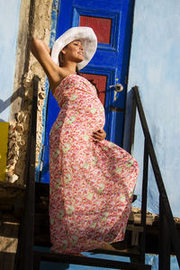 Pregnant woman poses in front of a caribbean facade enjoying the sunlight at sunset