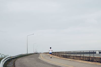 Rear view of man jogging on bridge against sky