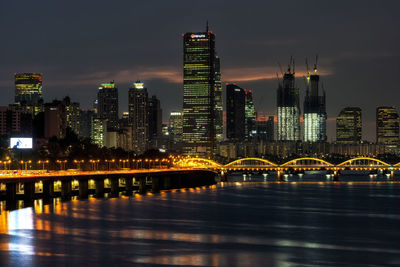 Illuminated city by river against sky at night