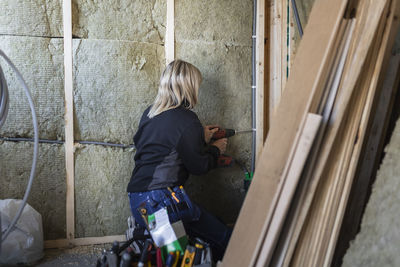 Blond female technician with drill machine drilling wall