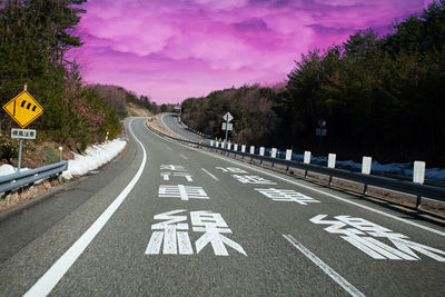 Road sign by trees against sky