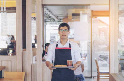 Portrait of waiter holding tray with food at restaurant