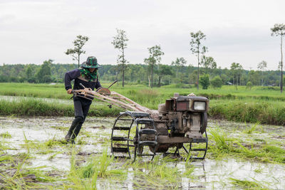 Farmer farming at rice paddy against sky