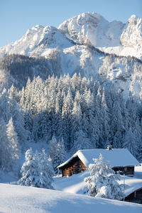 Winter nature scenery with snowcapped wooden hut and snowy mountains in the background
