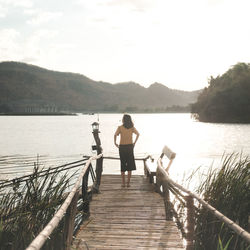 Rear view of man on pier over lake against sky