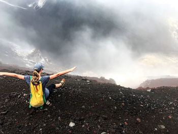 Rear view of mature woman crouching on mountain during foggy weather