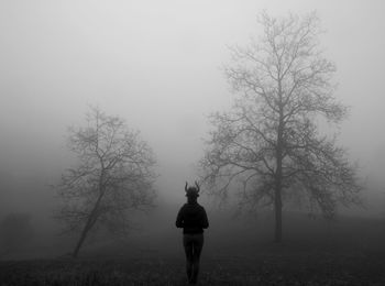 Rear view of woman standing on field against sky during foggy weather