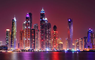 Illuminated modern buildings in city against sky at night