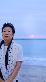 Woman looking away while standing at beach against sky during sunset