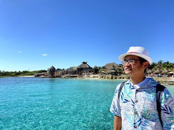 Man wearing hat standing by sea against blue sky