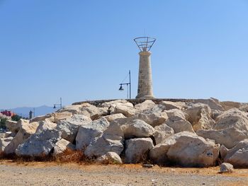 Lighthouse by rocks against clear blue sky