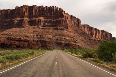 Road leading towards rocky mountains against sky