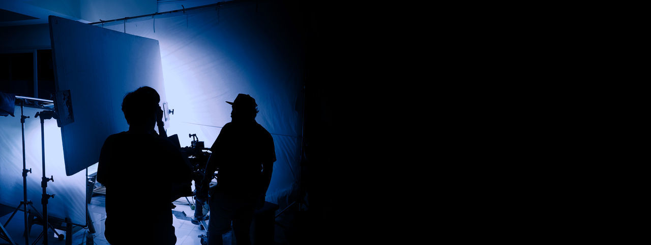 REAR VIEW OF SILHOUETTE MAN STANDING AGAINST BLUE WALL