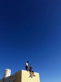 Low angle view of men standing against blue sky