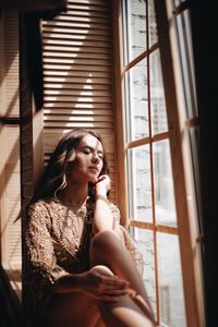 Close-up of young woman sitting by window at home