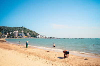 Group of people at beach against clear blue sky