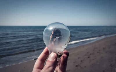 Human hand holding crystal ball on beach