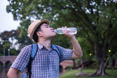 Man drinking water from bottle against tree