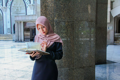 Young woman wearing hijab while turning page of holy book at mosque