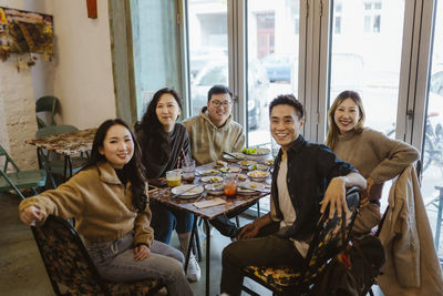 Portrait of happy male and female friends sitting together at restaurant