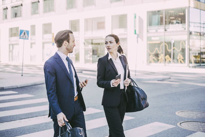 Business colleagues talking while crossing road in city