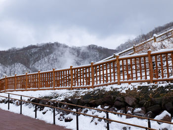 Snow covered railing by mountain against sky