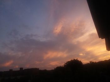 Low angle view of silhouette trees and buildings against dramatic sky