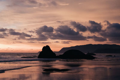 Silhouette rocks on shore against sky during sunset