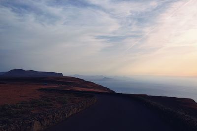 Road by sea against sky during sunset