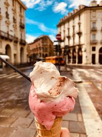 Cropped hand of person holding ice cream cone against buildings