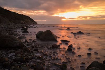 Rocks on beach against sky during sunset