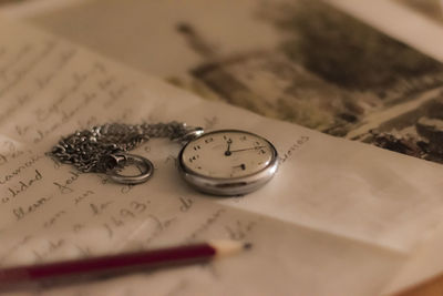 Close-up of pocket watch and pencil on paper