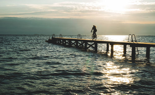 Silhouette person on pier over sea against sky during sunset