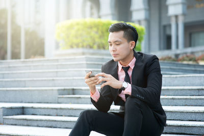 Young businessman using phone on staircase in city