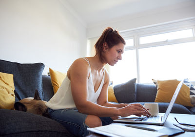 Young woman using mobile phone while sitting on sofa