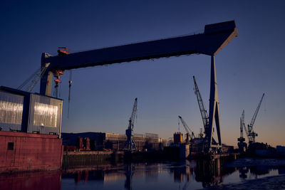 Cranes at pier against sky during sunset