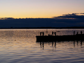 Silhouette people on pier by lake against sky during sunset