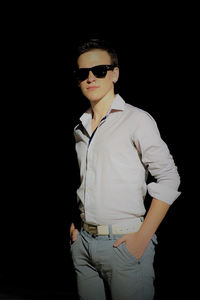 Young man wearing sunglasses standing against black background