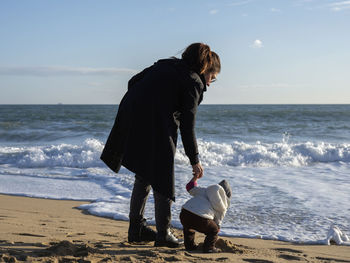 Full length of mother and daughter on beach against sky