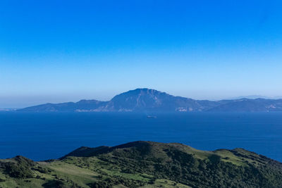 Scenic view of sea and mountains against clear blue sky